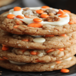 Freshly baked carrot cake cookies topped with cream cheese frosting, cooling on a rack in a cozy kitchen setting.